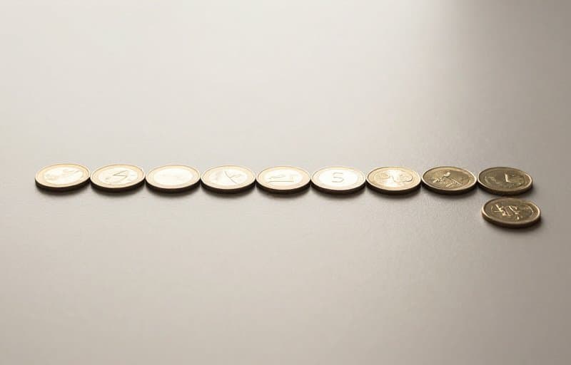 A neat row of twelve identical coins with three at the end sliding out of line, illustrating an annual subscription refund pulling months of payment back out