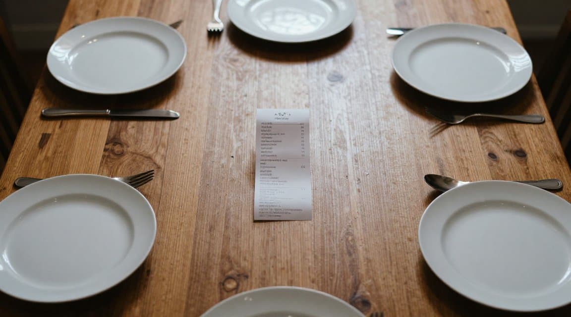 A single paper receipt at the center of a dining table set for six, standing in for how one payment behind a Family Sharing refund can cover six people